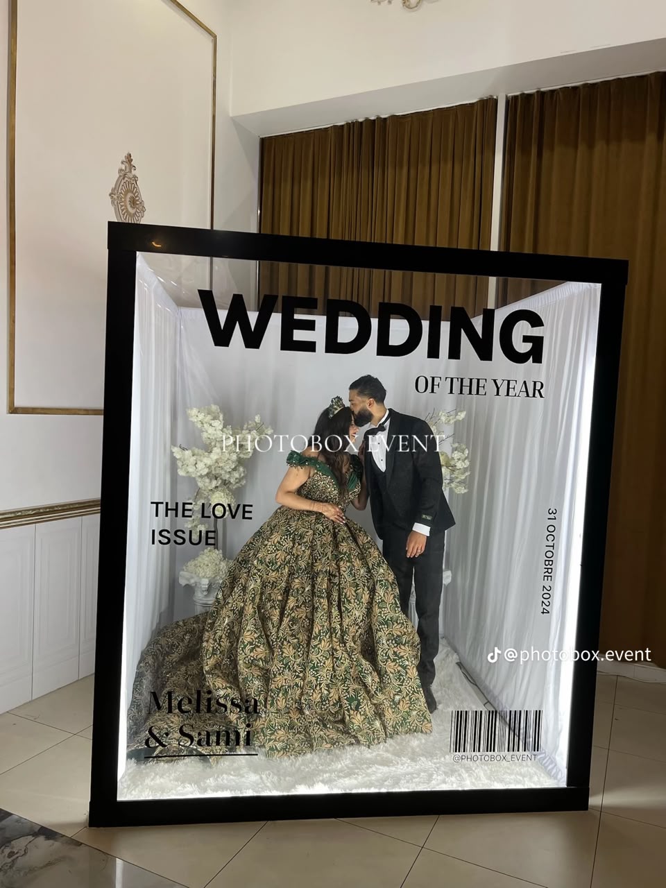 A couple posing inside a magazine-cover booth at an indoor wedding